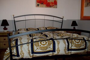 Uma cama com estrutura de metal, duas luminárias de cabeceira e um quadro com flores na parede.