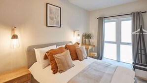 A neatly arranged bedroom with a bed, bedside tables, a dresser, and a window with curtains. - Host & Stay | Skyline Apartment (Whitby)