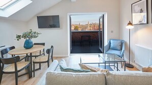 A modern living room with a sofa, coffee table, and chairs. There is a balcony with a view of the city. - Host & Stay | Skyline Apartment (Whitby)