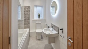 A modern bathroom with a bathtub, toilet, and sink. - Host & Stay | Skyline Apartment (Whitby)