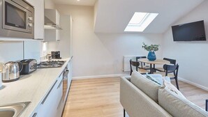 A modern kitchen with a built-in microwave, gas stove, and kettle. There is a dining area with a table and chairs, and a sofa in the living area. - Host & Stay | Skyline Apartment (Whitby)