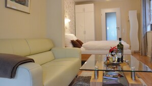 A modern living room with a glass coffee table, a sofa, a bed with white bedding, and a wardrobe.