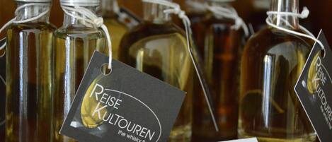 Several glass bottles with metal caps, each with a tag. One tag reads 'Reise Kulturen the whisky flat.' Another tag says 'Single Cask / Scotch.'