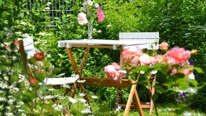 A garden setting with a white table and chairs, surrounded by lush greenery and flowers.