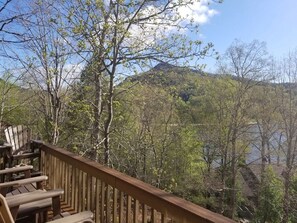 A wooden deck with chairs overlooking a forested area and a body of water.