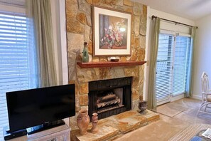 A living room with a stone fireplace, a flat-screen TV, and a framed floral artwork above the mantel.