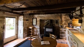 Interior rústico de piedra con una mesa de madera, sillas, chimenea y un pequeño armario de madera.