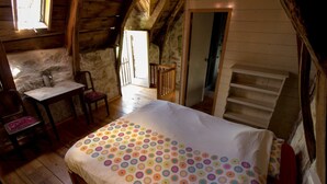 Un dormitorio acogedor en el ático, con piso de madera, una cama con colcha alegre de lunares, una mesita con silla y una escalera que sube a un nivel superior.