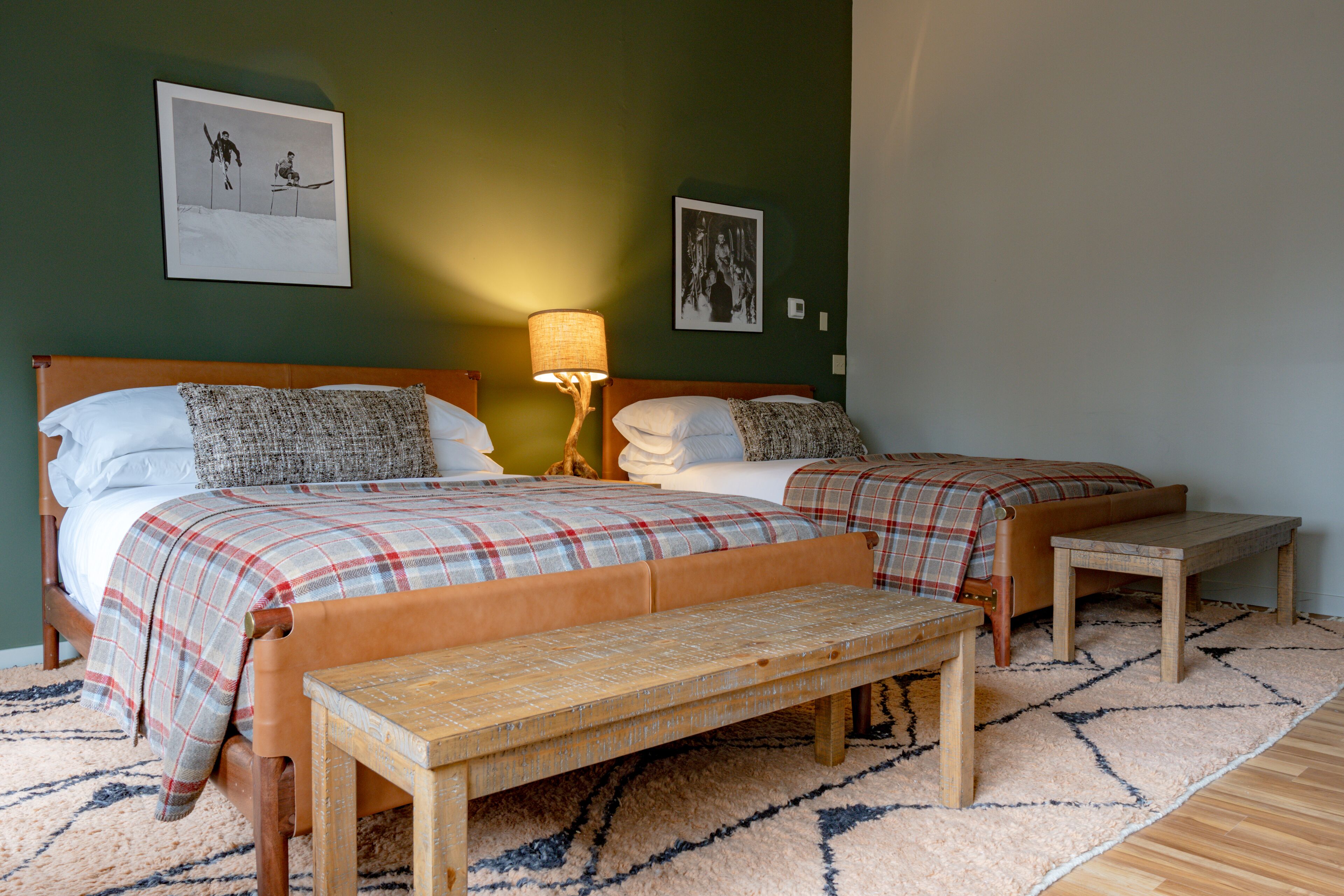 A double bed with a plaid bedspread, a bedside table with a lamp, and a bench in a hotel room.
