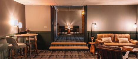 Ein Hotelzimmer mit Teppichboden, einer Couch, einem Esstisch mit Stühlen, einer Lampe und Blick durch eine Tür.