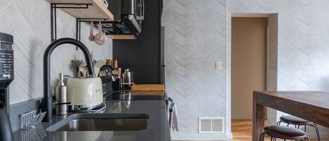 Una cocina moderna con encimera negra, pileta de acero inoxidable y taburetes de madera.