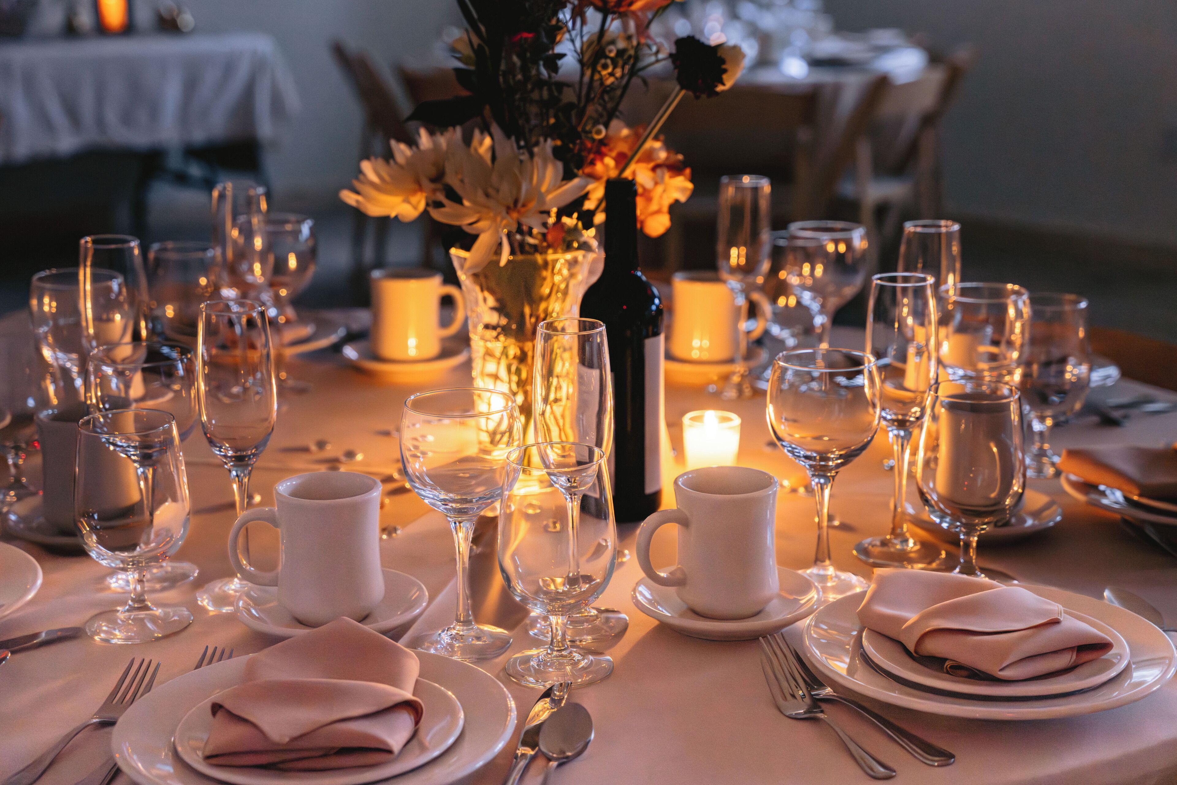 A table set for a meal with wine glasses, plates, and a vase of flowers.