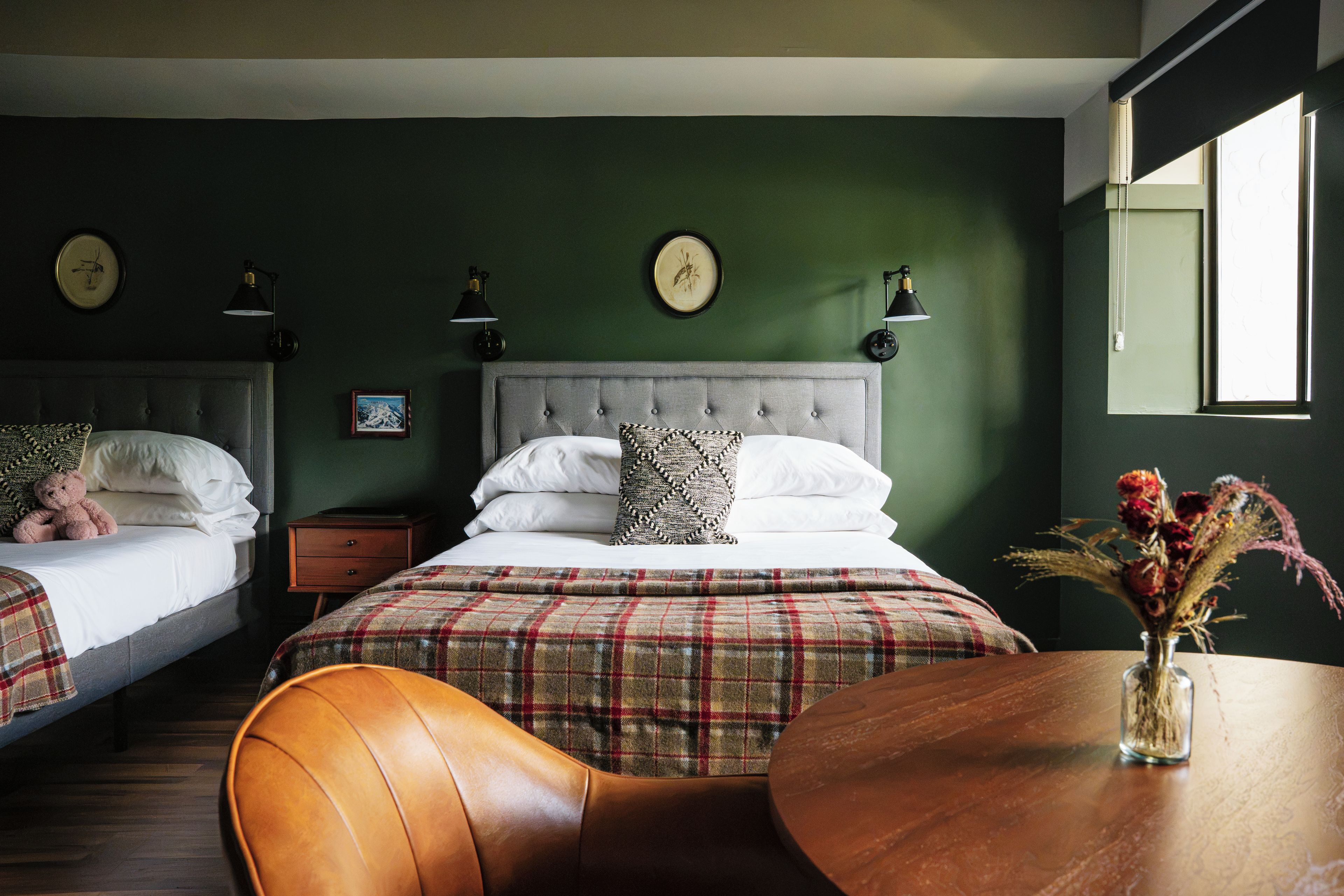 A bedroom with two beds, a wooden nightstand, a round wooden table, and a vase with flowers.
