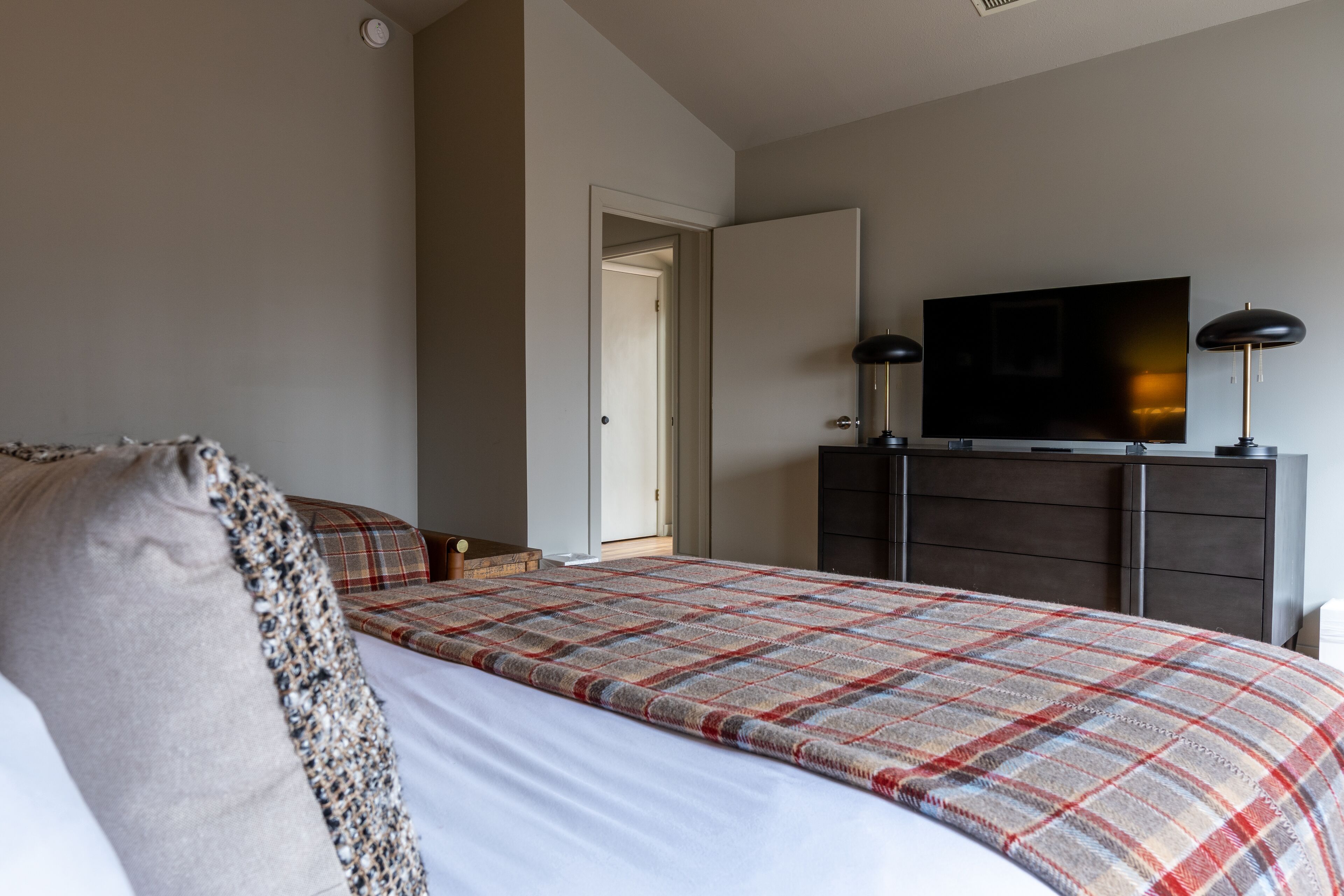 A bedroom with a bed, a television on a dresser, and a door leading to another room.