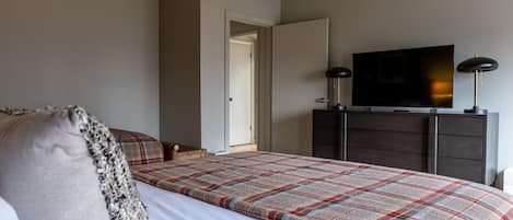 A bedroom with a bed, a television on a dresser, and a door leading to another room.