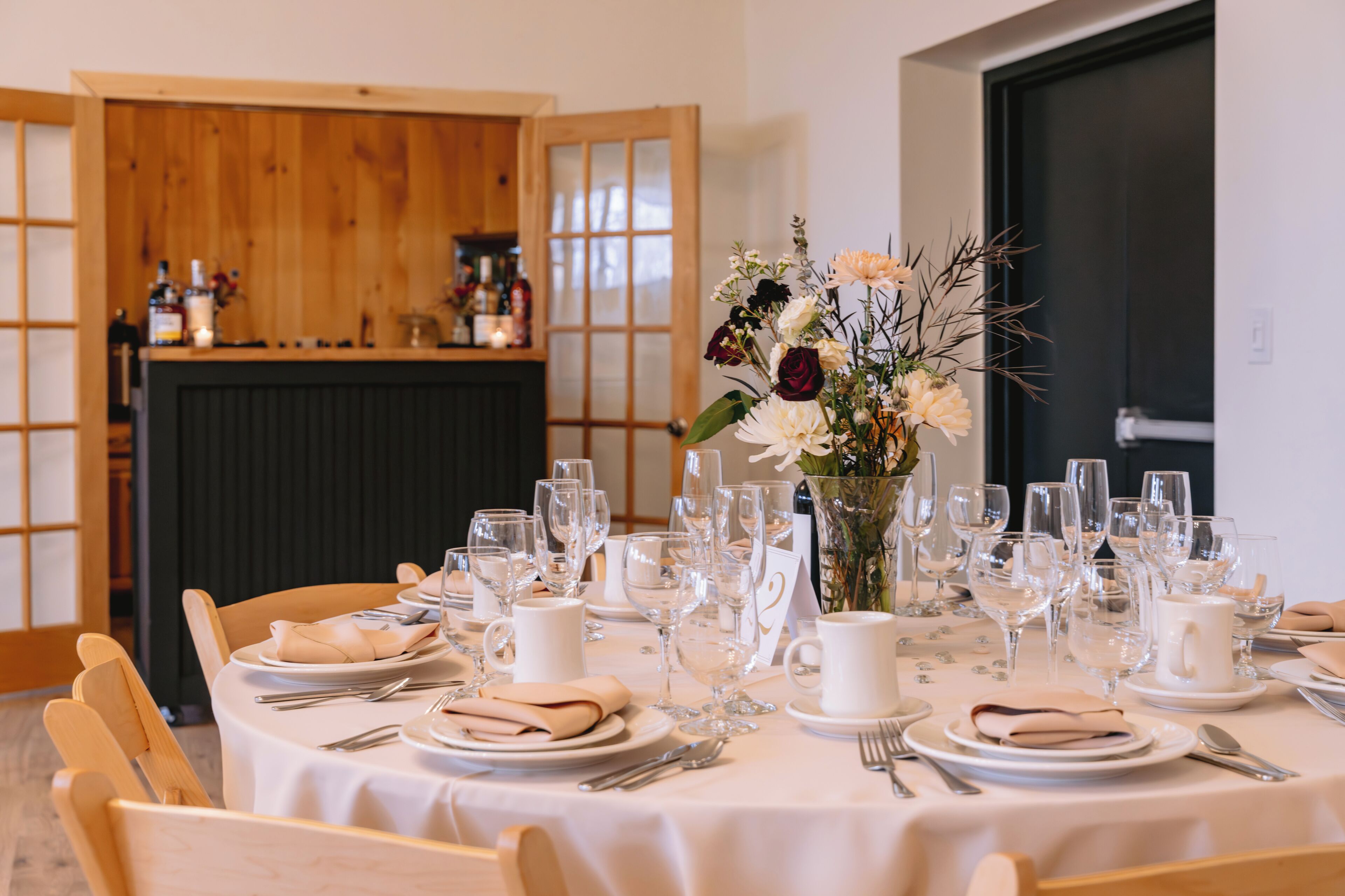 Une table à manger dressée avec une nappe blanche, des assiettes, des verres et un vase rempli de fleurs.