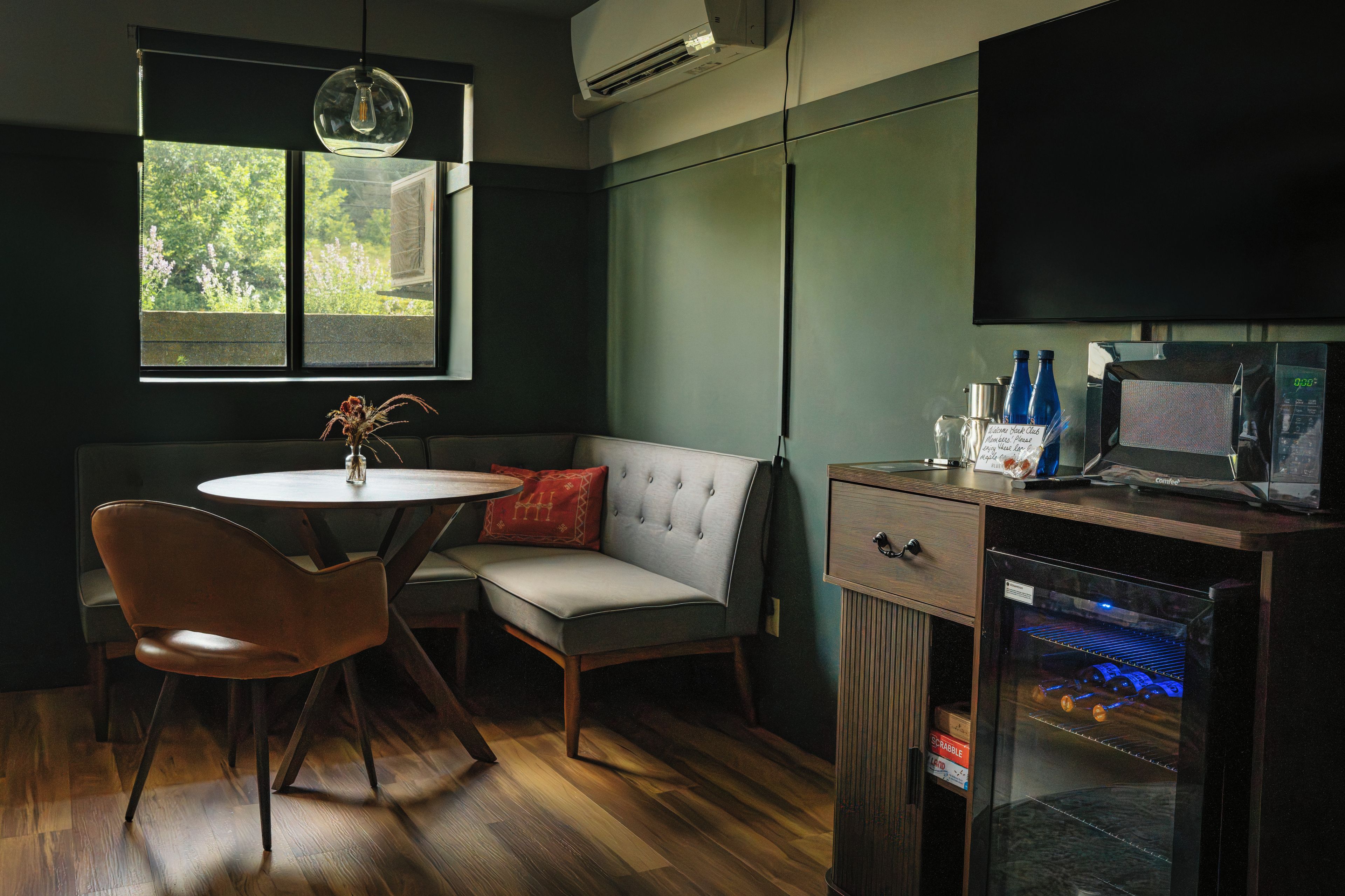 A room with a round table, a cushioned bench, a television, and a coffee machine.