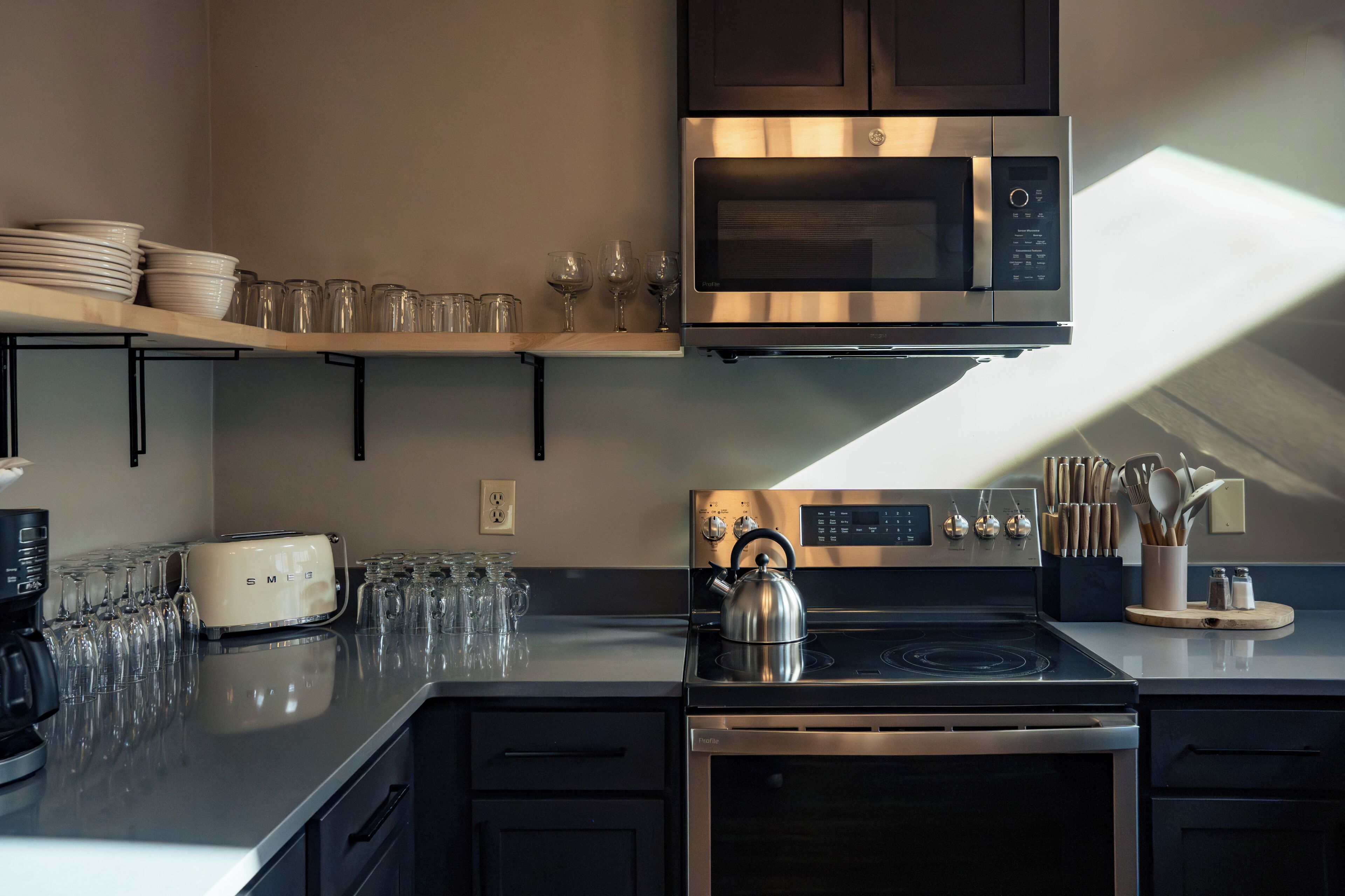 A modern kitchen with a stainless steel microwave, toaster, kettle, and oven.