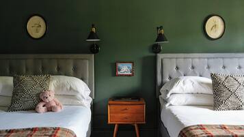 A bedroom with two beds, a nightstand, wall-mounted lamps, and a framed picture.