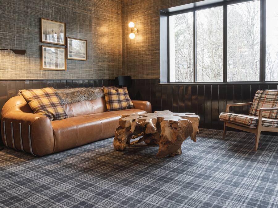 Une pièce chaleureuse avec un canapé en cuir, des coussins à motifs écossais, une table basse en bois et un fauteuil à motifs écossais.