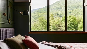Un dormitorio con un ventanal que ofrece vistas a una montaña boscosa.