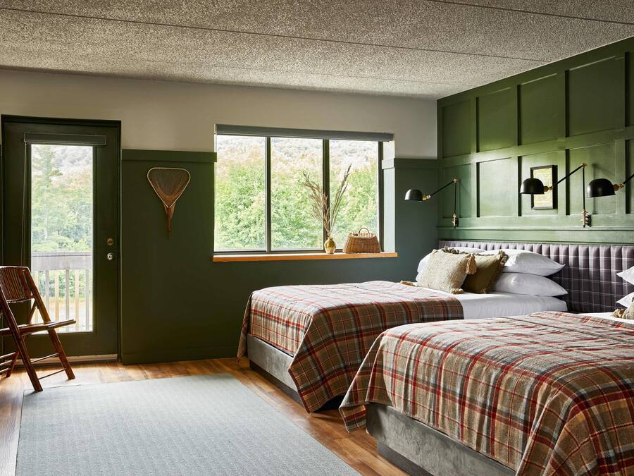 Une chambre avec deux lits, une fenêtre, une chaise et une lampe fixée au mur.
