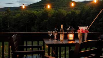 Una terraza de madera con una mesa dispuesta para cenar, que incluye una botella de vino, copas y un farol.