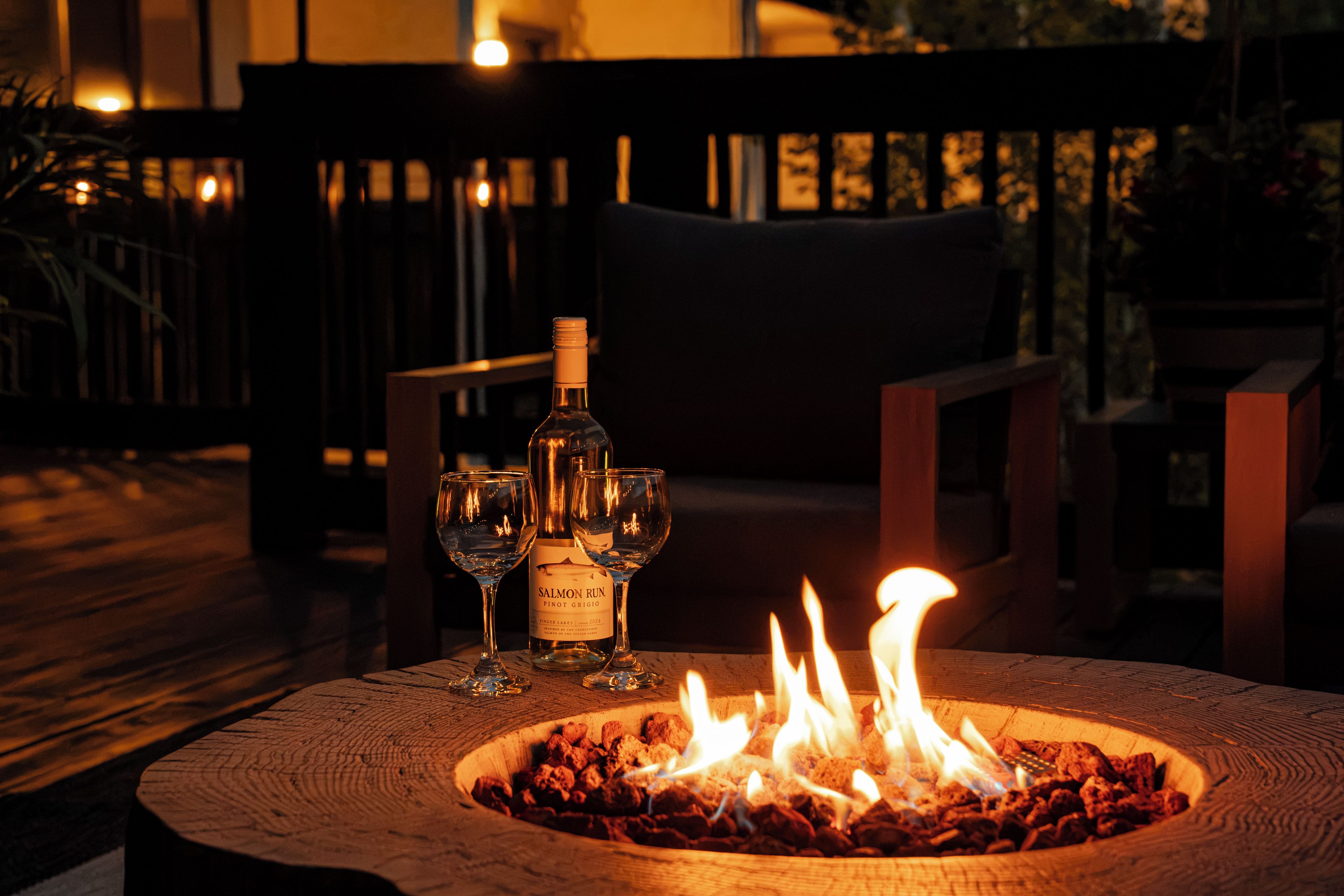 Una mesa de madera con una botella de vino, dos copas y un brasero encendido.
