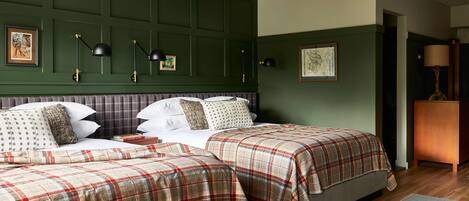 A room with two beds, each with a plaid bedspread, a headboard, and a bedside table with a lamp.