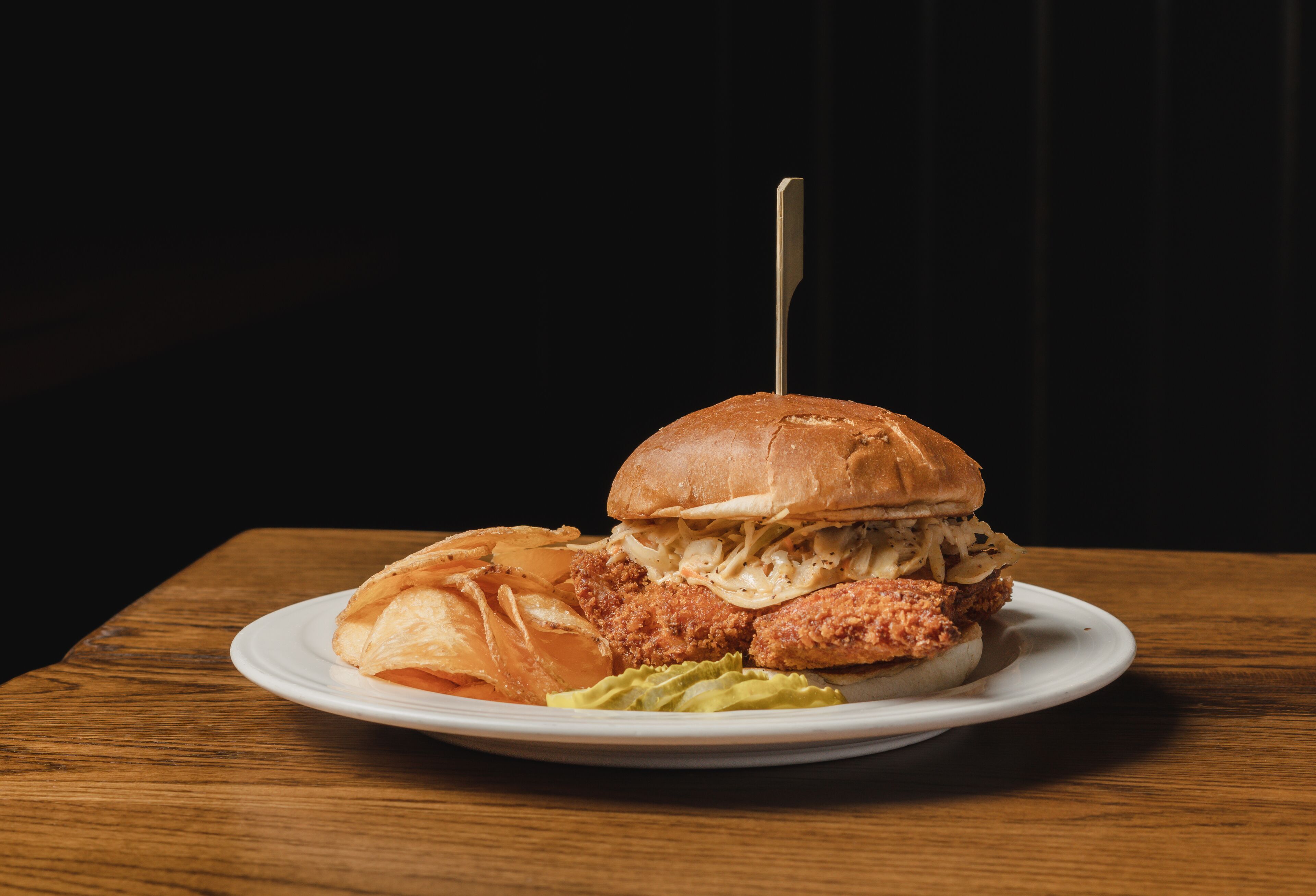 A plate with a sandwich, chips, and a side of coleslaw on a wooden table.