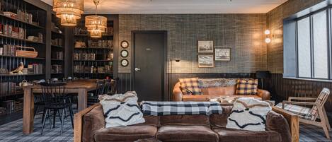 Un salon chaleureux avec un canapé en cuir marron, une table basse en bois et un coin repas comprenant une table et des chaises en bois. On y trouve également des étagères remplies de livres et une cheminée.