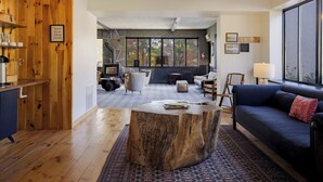 Una sala de estar moderna con un gran ventanal, un sofá azul, una mesa de centro de madera y una pared rústica de madera.