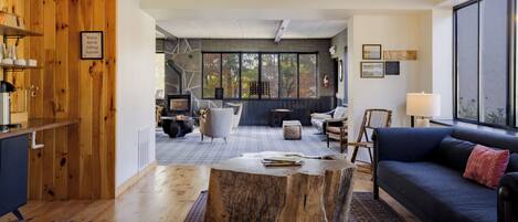 A modern living room with a large window, a blue sofa, a wooden coffee table, and a rustic wooden wall.