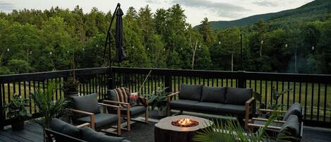 A deck with outdoor furniture, a fire pit, and a view of a forested area.