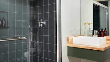 Ein modernes Badezimmer mit Duschabtrennung aus Glas, einem weißen Waschbecken mit Holzbeschlag und einem Spiegel darüber.