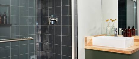 A modern bathroom with a glass shower enclosure, a white sink with a wooden countertop, and a mirror above the sink.