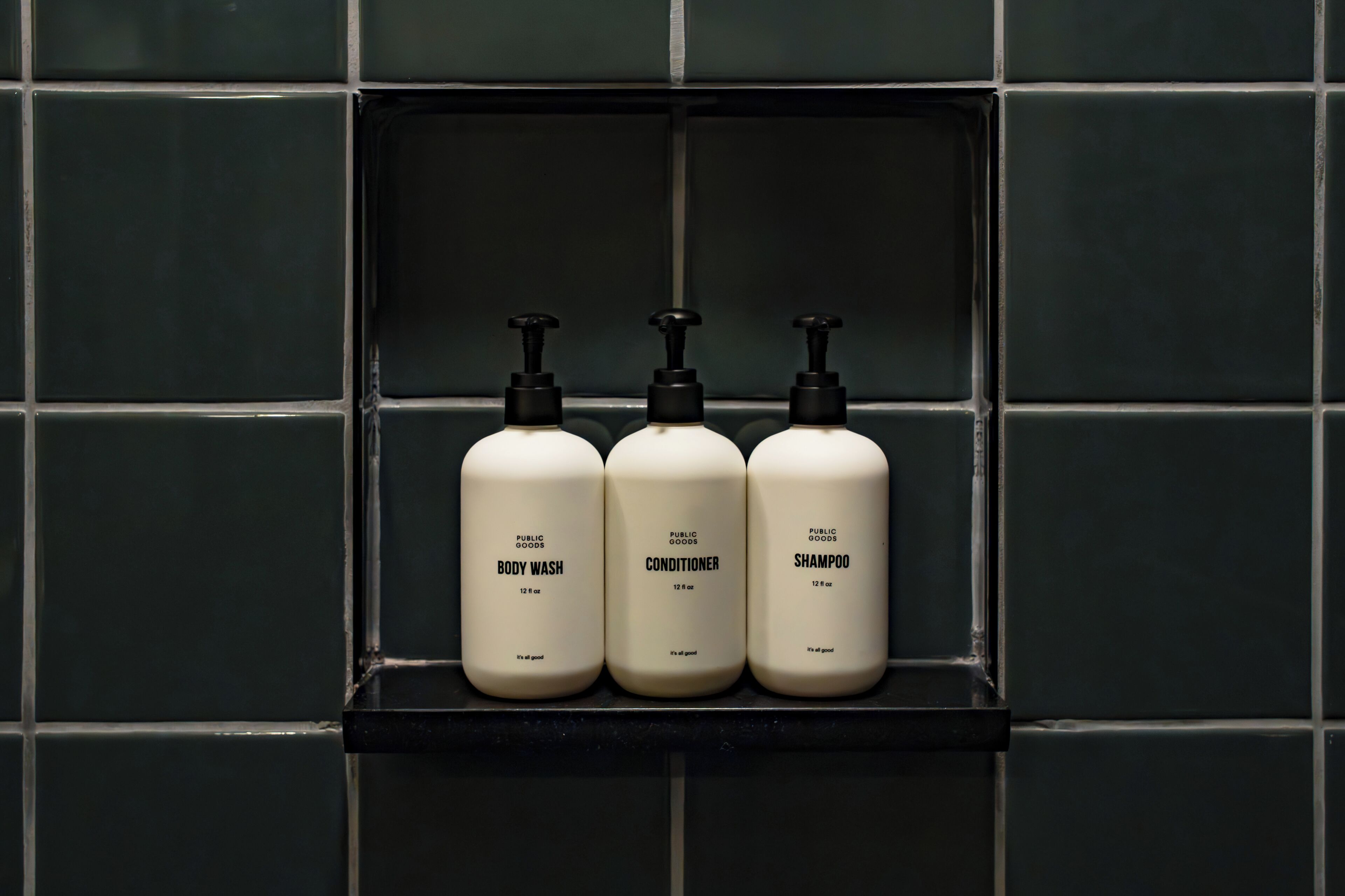 Three bottles of body wash, conditioner, and shampoo on a shelf against a tiled wall.