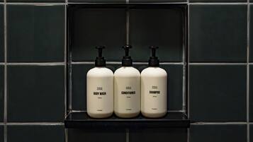 Three bottles of body wash, conditioner, and shampoo on a shelf against a tiled wall.