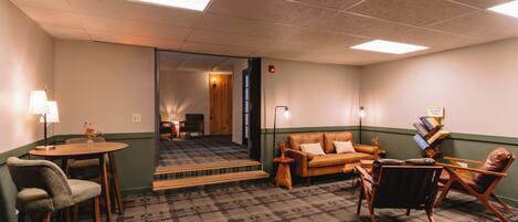 A hotel room with a checkered carpet, a sofa, a chair, a small table, and a lamp.