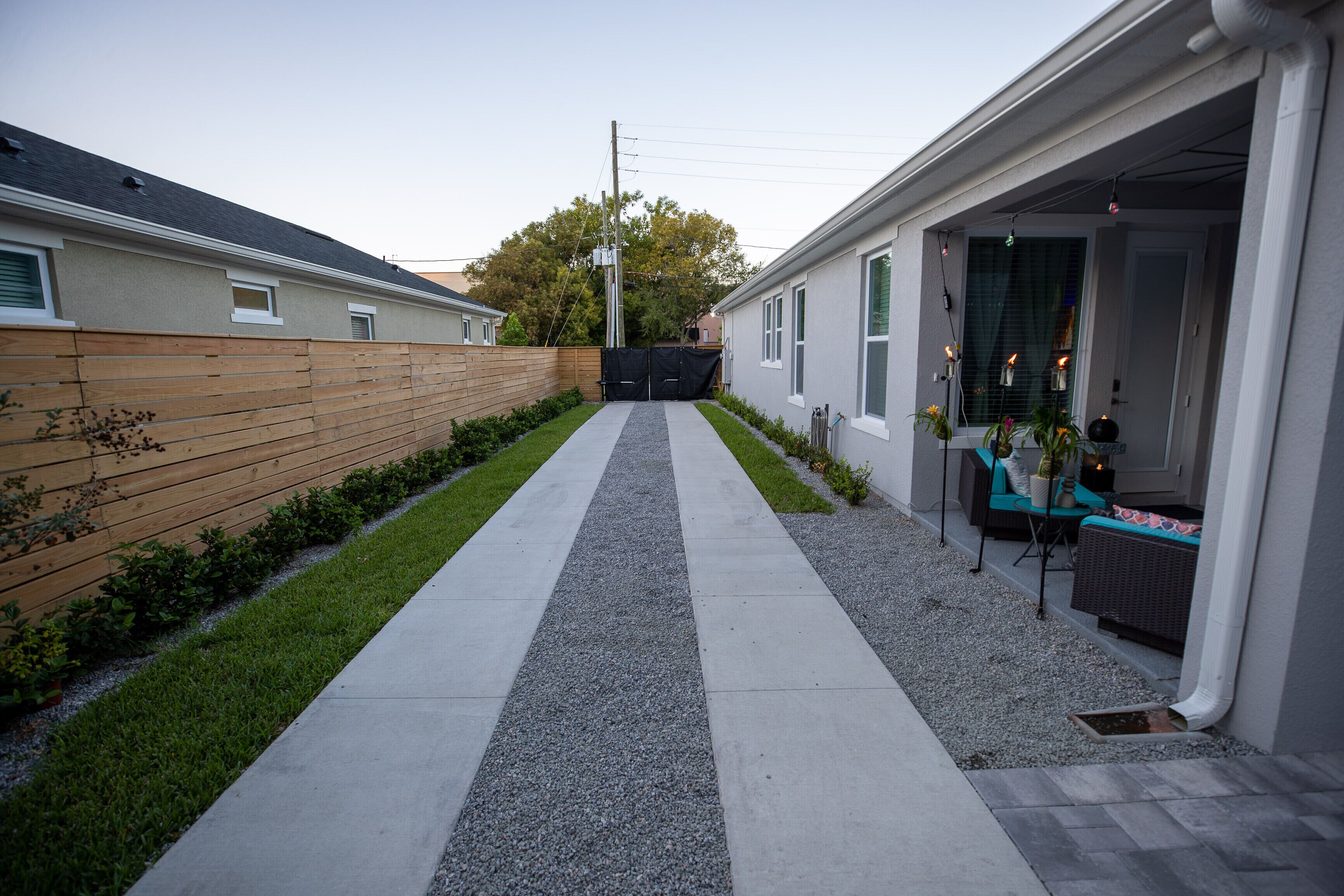 A pathway leading to a house with a wooden fence, a gravel area, and a small garden.