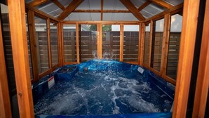 Uma banheira de hidromassagem dentro de um gazebo de madeira com telhado inclinado.