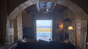 A cozy room with a stone archway, a fireplace, a large bed, and a view of the sea.