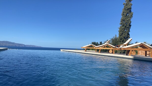 A poolside area with wooden lounge chairs and a clear view of the sea.