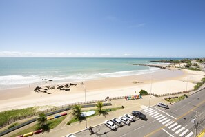 A coastal road with a beach on one side and a parking lot with cars. - Apto Vista Mar em Areia Preta Natal (Natal)