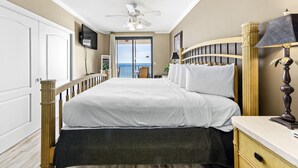 Une chambre d’hôtel équipée d’un lit, d’une table de chevet, d’une lampe, d’un ventilateur de plafond, d’une télévision et offrant une vue sur l’océan grâce à une porte coulissante.