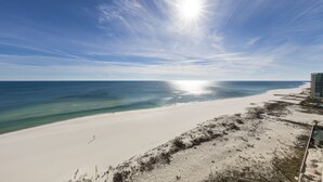 Une plage avec un ciel dégagé, un rivage sablonneux et un bâtiment visible au loin.