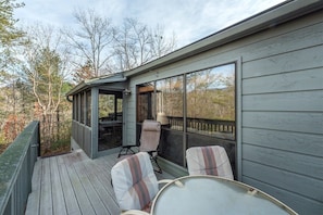 A covered deck with outdoor furniture and large windows.