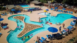 Ein großes Schwimmbecken im Freien mit mehreren Bahnen und einem separaten Planschbecken, umgeben von Liegestühlen und Sonnenschirmen.