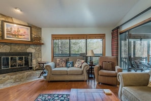 A cozy living room with a stone fireplace, a large window with a view, and a comfortable seating area.