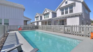 Une piscine entourée d’une clôture en bois, avec un bâtiment blanc en arrière-plan.